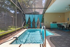 Ein Swimmingpool mit Metallgeländer, eine überdachte Terrasse mit Tisch und Stühlen und ein Blick auf einen Garten mit Zaun und Bäumen.