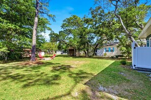A residential property with a well-maintained lawn, a small shed, and a house with a white exterior and blue trim. - Charming OKI Cottage Walking Distance to Beach! (Oak Island)