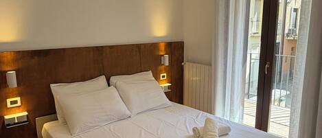 A hotel room with a large bed, two bedside tables with lamps, a wooden headboard, and a view of the outside through a glass door.