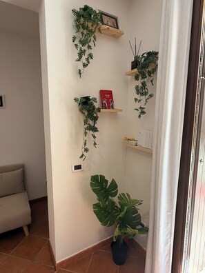 Ein Wohnzimmer mit einer Couch, einem Blumentopf und an der Wand befestigten Regalen mit Pflanzen und einem Buch.