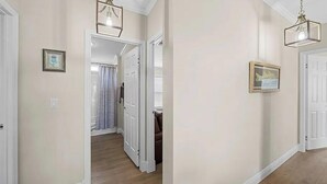 Um corredor com uma porta que dá para um quarto, um quadro na parede e um lustre.