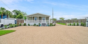 A single-story mobile home with a porch, surrounded by a gravel driveway and a wooden fence. - Terrific 3-bedroom house in Port St. Joe with boat and camper parking (Port St. Joe)
