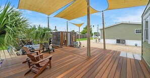 Eine Holzterrasse mit Sitzgelegenheiten im Freien, eine kleine Struktur und ein Gebäude im Hintergrund.