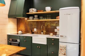 Una cocina con armarios verdes, un lavamanos blanco y un refrigerador blanco.