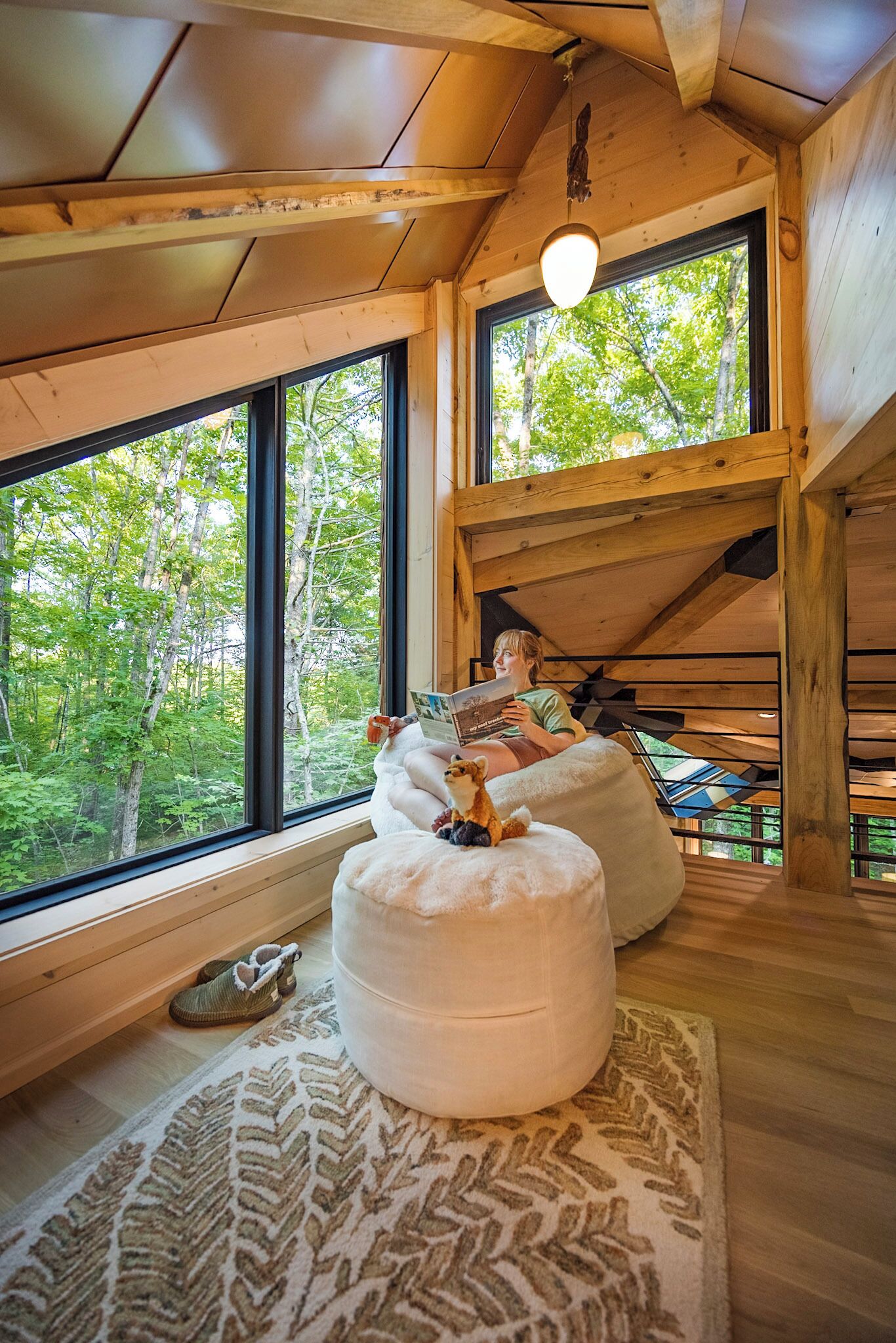 Ein gemütliches Blockhaus-Interieur mit großen Fenstern, Holzbalkendecke und einer Person, die ein Buch liest.