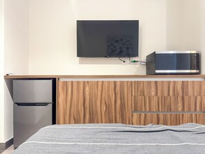 Une petite cuisine équipée d’un four à micro-ondes, d’un petit réfrigérateur et d’un téléviseur à écran plat fixé au mur.