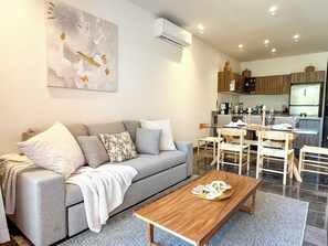 A modern living room with a grey sofa, wooden coffee table, and a dining area with a glass table and chairs. - 3BR Tulum Jungle Retreat with Private Patio (Tulum)