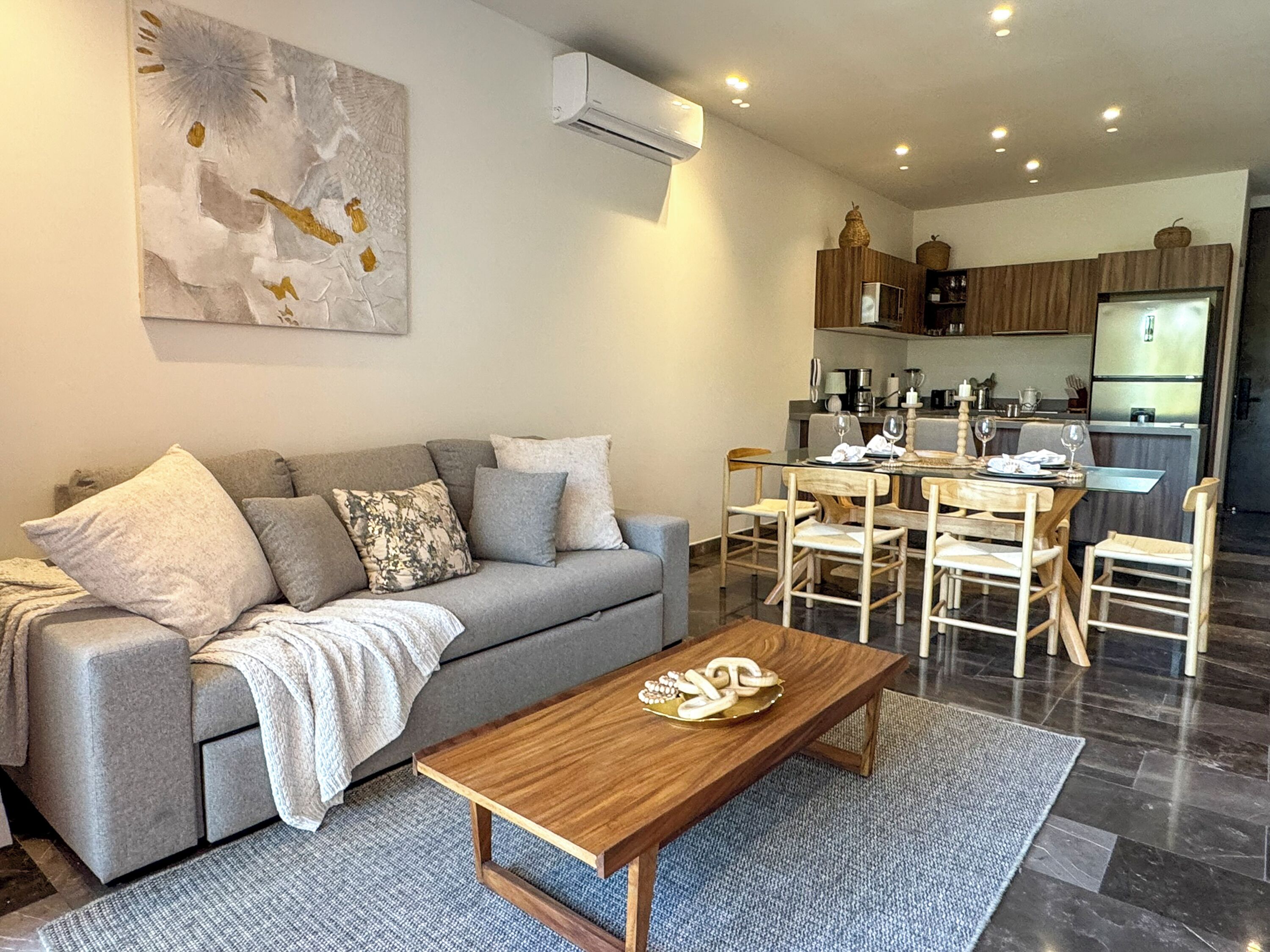 A modern living room with a grey sofa, wooden coffee table, and a dining area with wooden chairs.