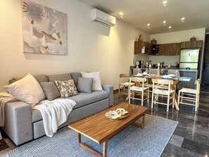 Un salon moderne avec un canapé gris, une table basse en bois et un coin repas avec des chaises en bois.