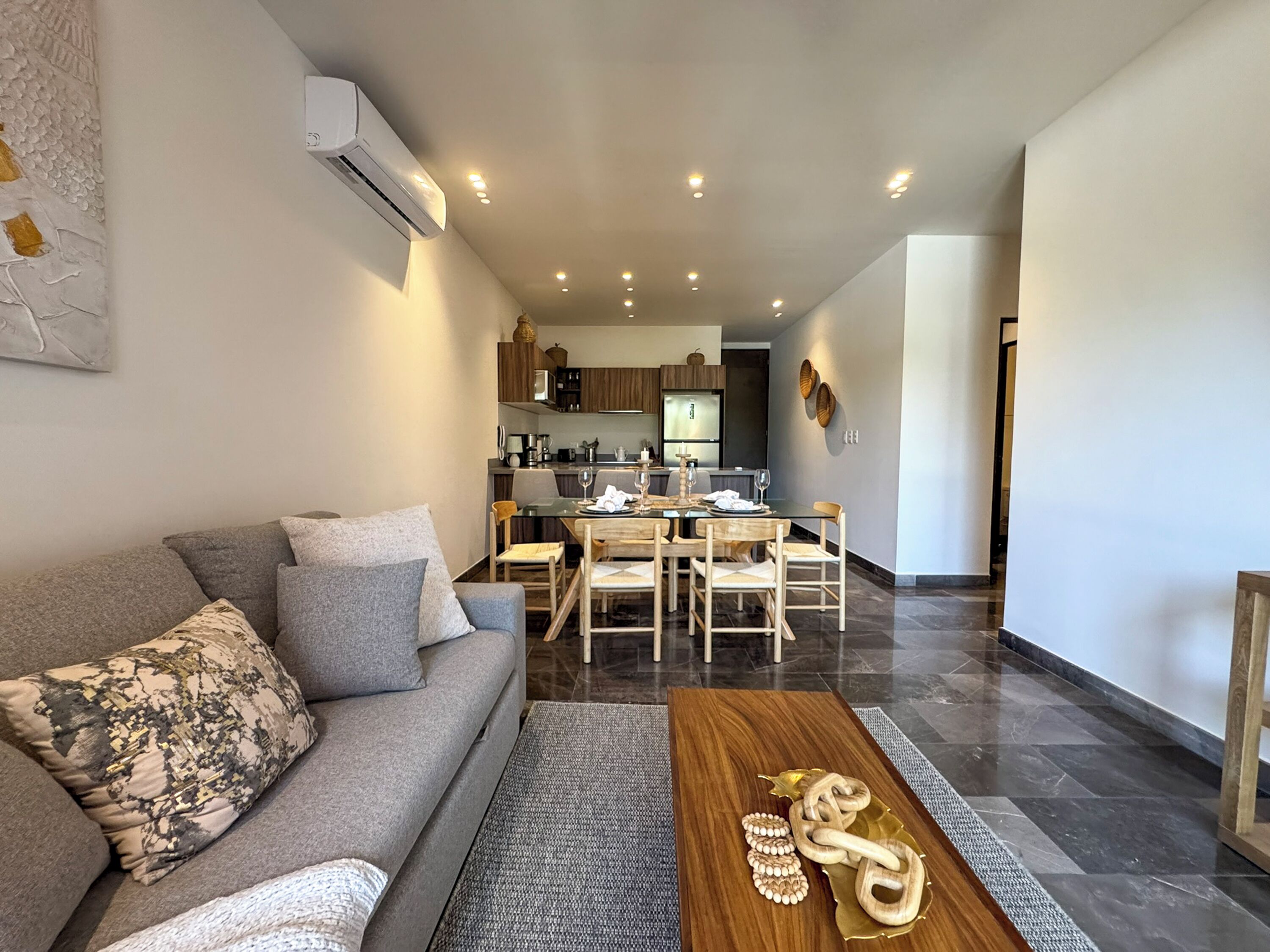 A modern living room with a grey sofa, wooden coffee table, and a dining area with a wooden table and chairs.
