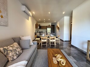 A modern living room with a grey sofa, wooden coffee table, and a dining area with a wooden table and chairs. - 3BR Tulum Jungle Retreat with Private Patio (Tulum)