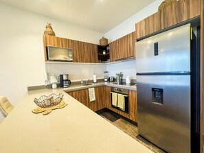 A modern kitchen with wooden cabinets, stainless steel appliances, and a central island with a woven placemat. - 3BR Tulum Jungle Retreat with Private Patio (Tulum)