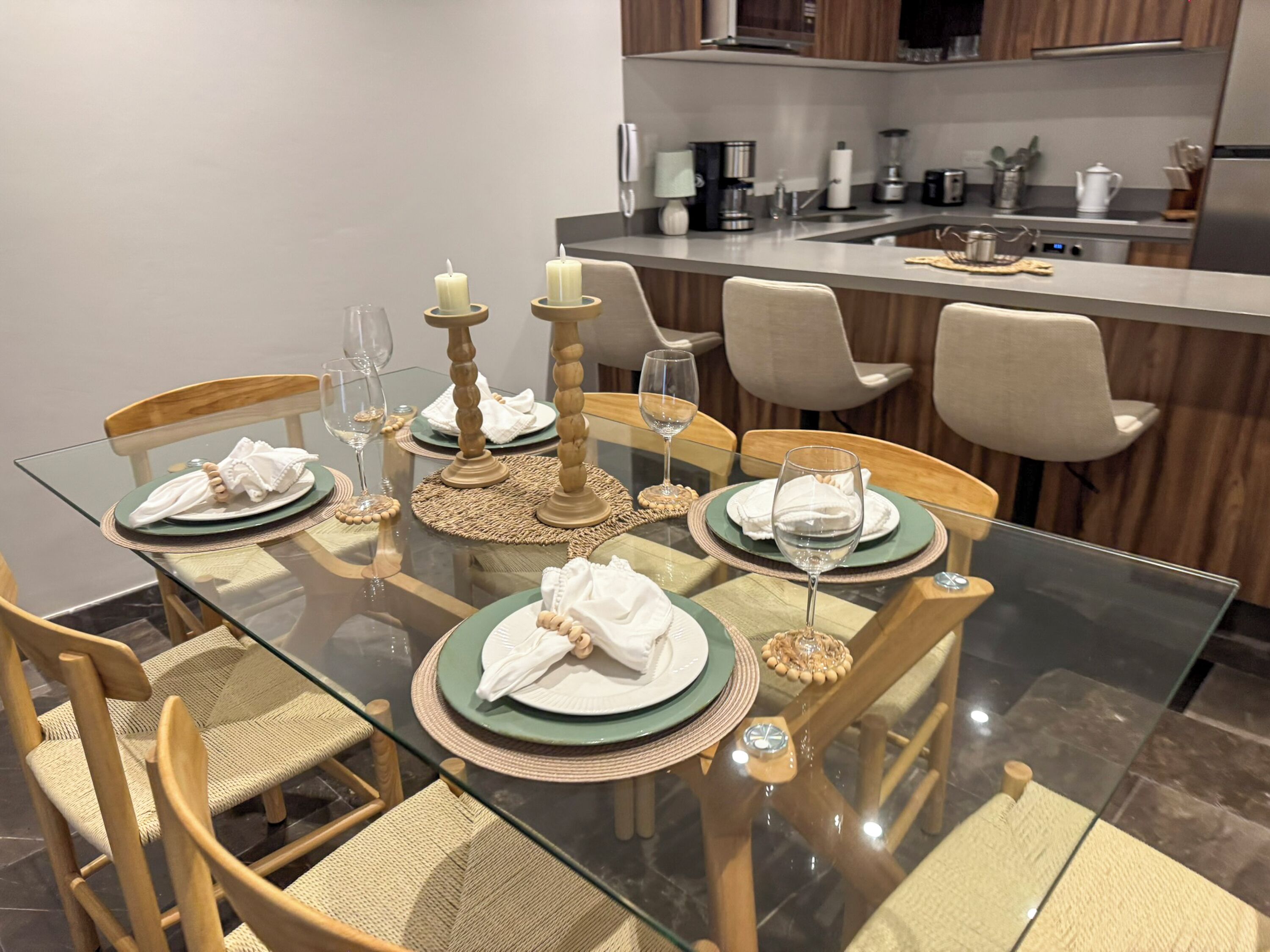 A dining area with a glass table, woven placemats, and wooden chairs.