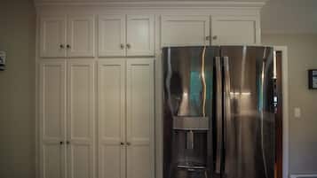 A stainless steel refrigerator with a water dispenser, white cabinetry, and a patterned floor.