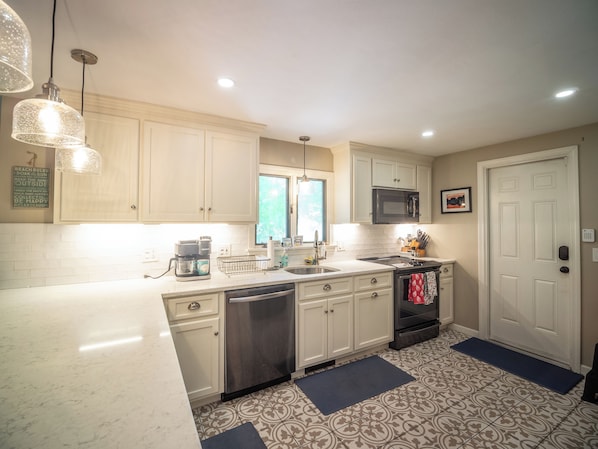 A kitchen with white cabinets, a stainless steel dishwasher, a microwave, and a coffee maker. - Connecticut Beach Home (Old Lyme)