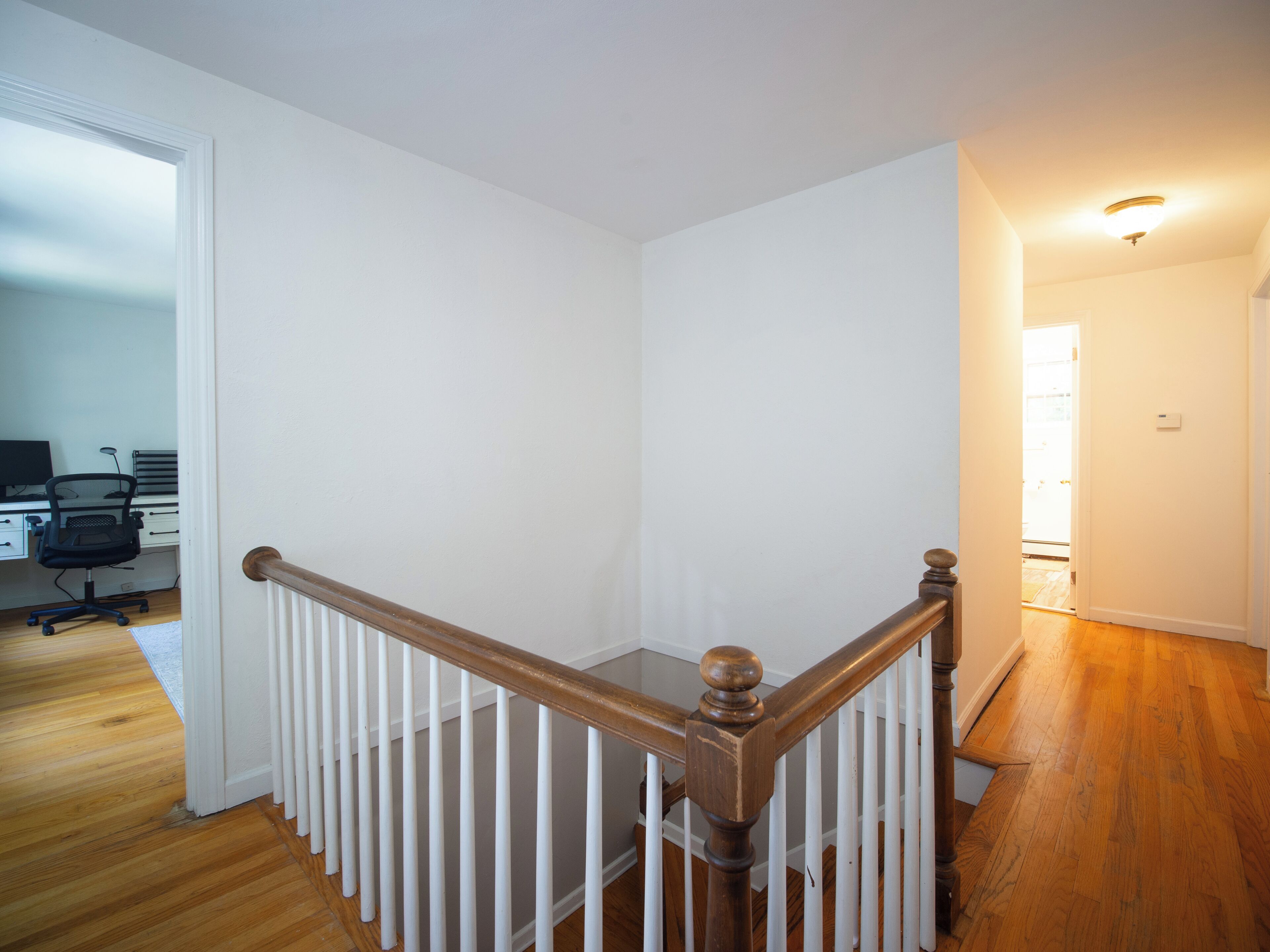 A staircase with a wooden handrail and white balusters, leading to a room with a white door and a computer desk with a chair.