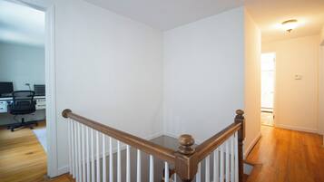 A staircase with a wooden handrail and white balusters, leading to a room with a white door and a computer desk with a chair.