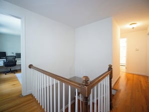 A staircase with a wooden handrail and white balusters, leading to a room with a white door and a computer desk with a chair. - Connecticut Beach Home (Old Lyme)