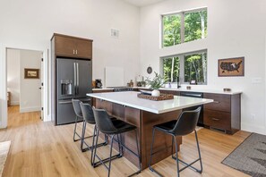 A modern kitchen with a central island, bar stools, and a large refrigerator. - !New!-Sunset Escape- Bayside Bluff with Hot Tub (Egg Harbor)