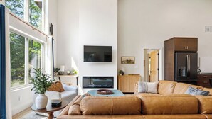 Ett vardagsrum med ett stort fönster, en platt-TV, en soffa och ett köksområde i bakgrunden.