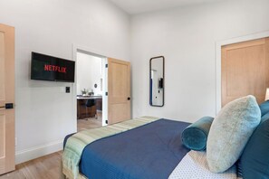 A bedroom with a bed, a television displaying 'NETFLIX,' a mirror, and a door leading to a bathroom. - !New!-Sunset Escape- Bayside Bluff with Hot Tub (Egg Harbor)