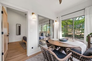 Ein modernes Zimmer mit Esstisch, Korbstühlen, einem großen Fenster mit Blick auf Grünflächen und einer Schiebetür zu einem weiteren Raum.