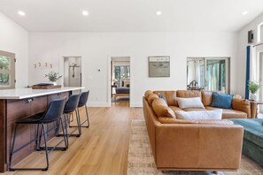 Ein modernes Interieur mit Küchenzeile, einer Sitzecke mit Sofa und Sesseln sowie Blick durch eine offene Tür.