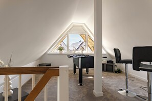 Ein modernes Schlafzimmer im Loft-Stil mit Schräge, einem Tischkicker, einem schwarzen Bürostuhl und einem Fenster mit Blick auf ein Nachbargebäude.