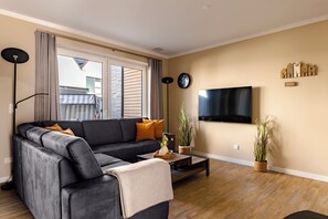 Una sala moderna con un sofá modular, un televisor de pantalla plana y un ventanal con cortinas.