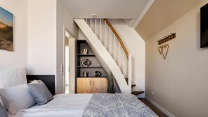 A bedroom with a bed, a wooden wardrobe, a staircase, and a wall-mounted TV. - A Getaway in Büsum - Vacation Home with Sauna & Fireplace (Büsum)