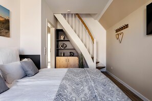 Ein Schlafzimmer mit einem Bett, einem Holzschrank, einer Treppe und einem an der Wand befestigten Fernseher.