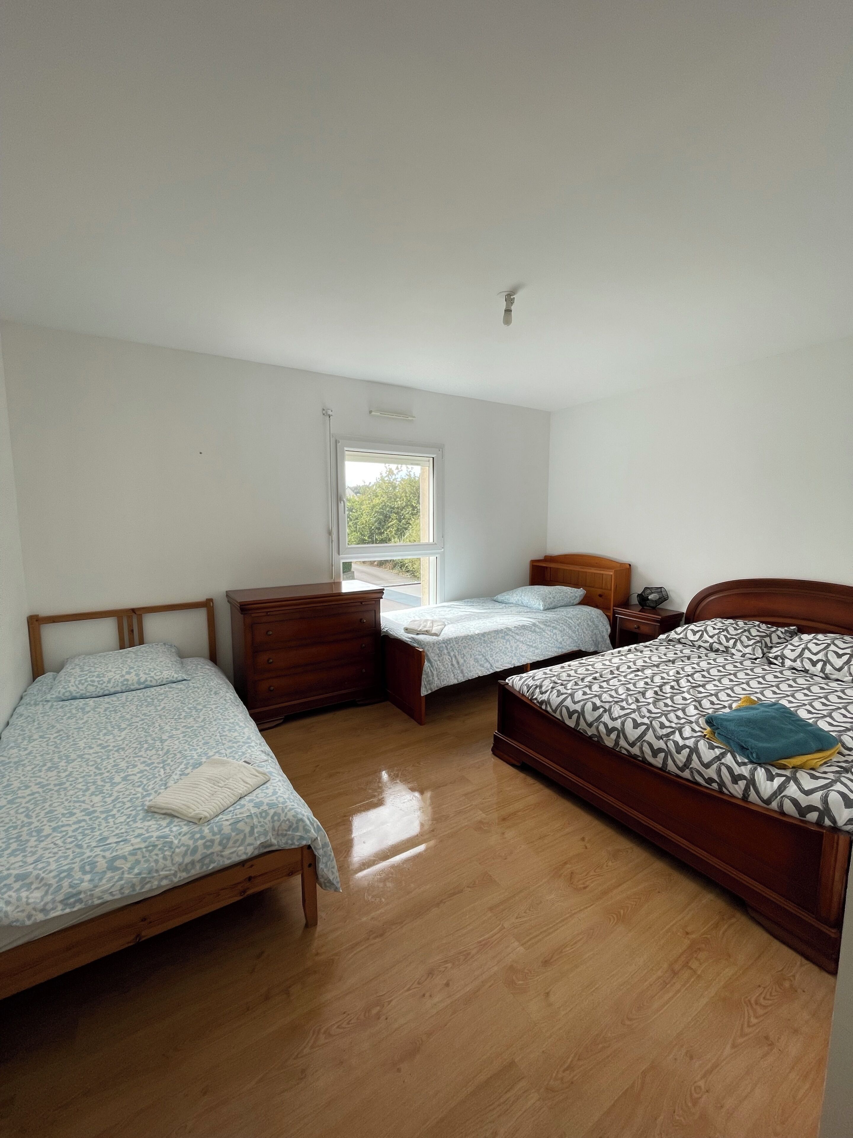 A bedroom with two single beds, a wooden dresser, and a window.