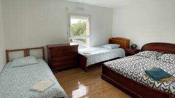 A bedroom with two single beds, a wooden dresser, and a window.