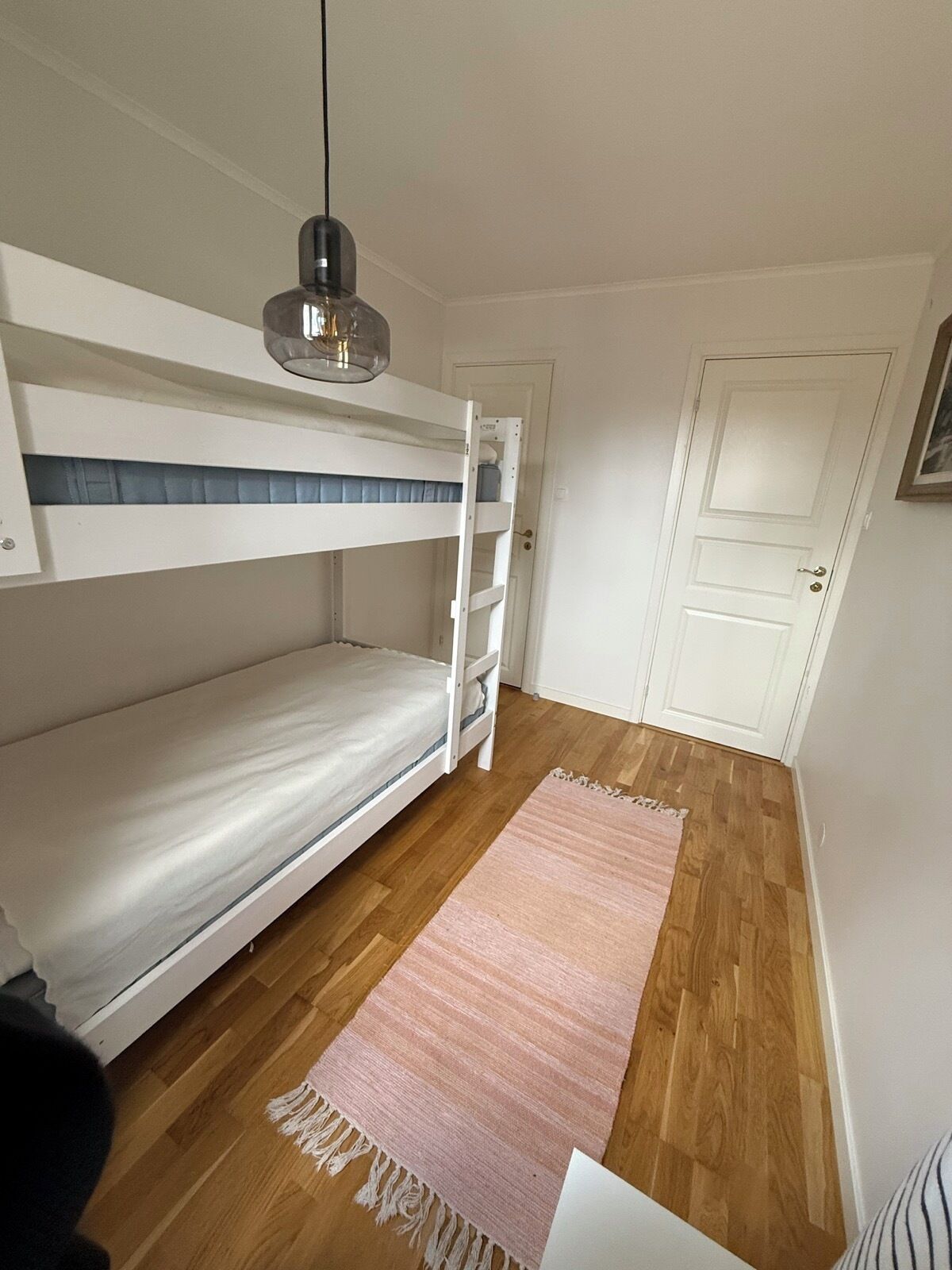 Et værelse med køjeseng, trægulv, hængende lampe og en dør.