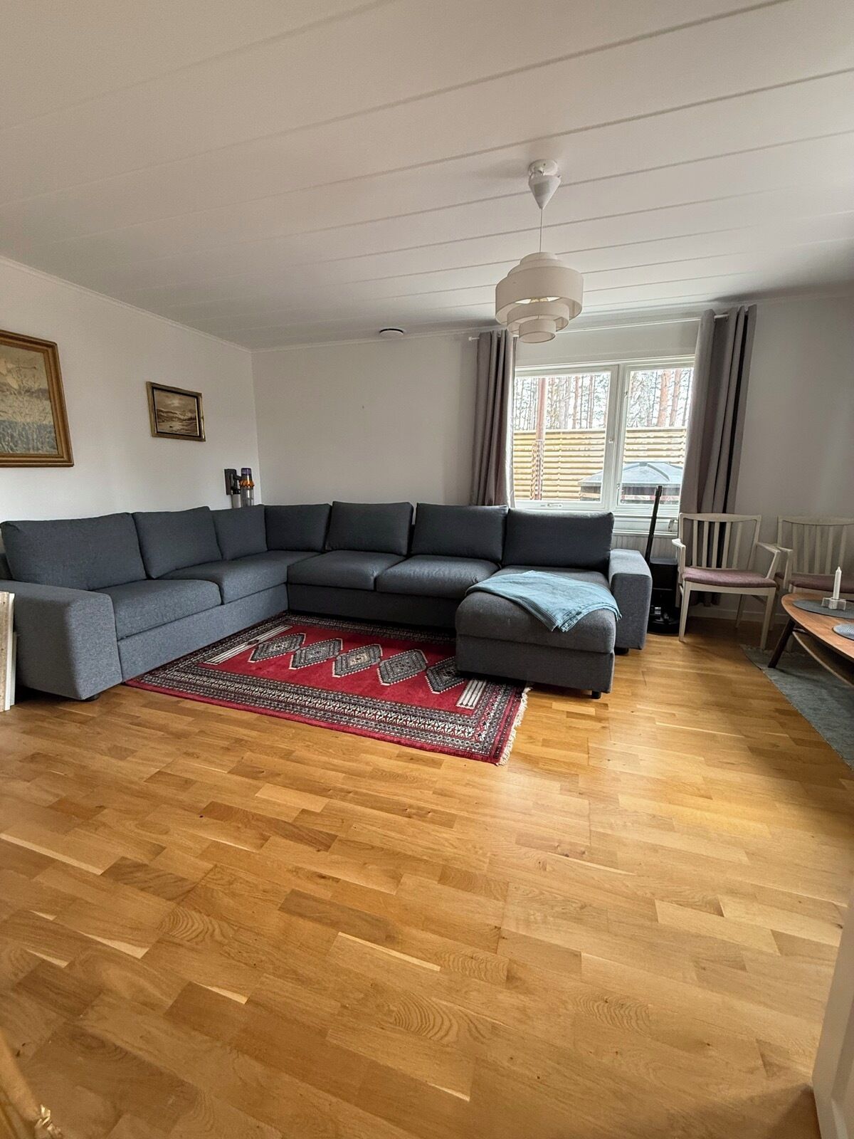 Ein modernes Wohnzimmer mit einem Ecksofa, einem roten Teppich mit Muster und Holzboden.