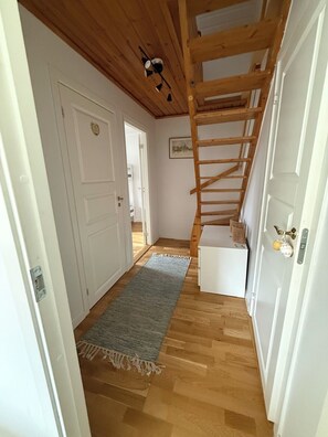 A hallway with wooden flooring, a grey rug, a white door, and a wooden staircase.