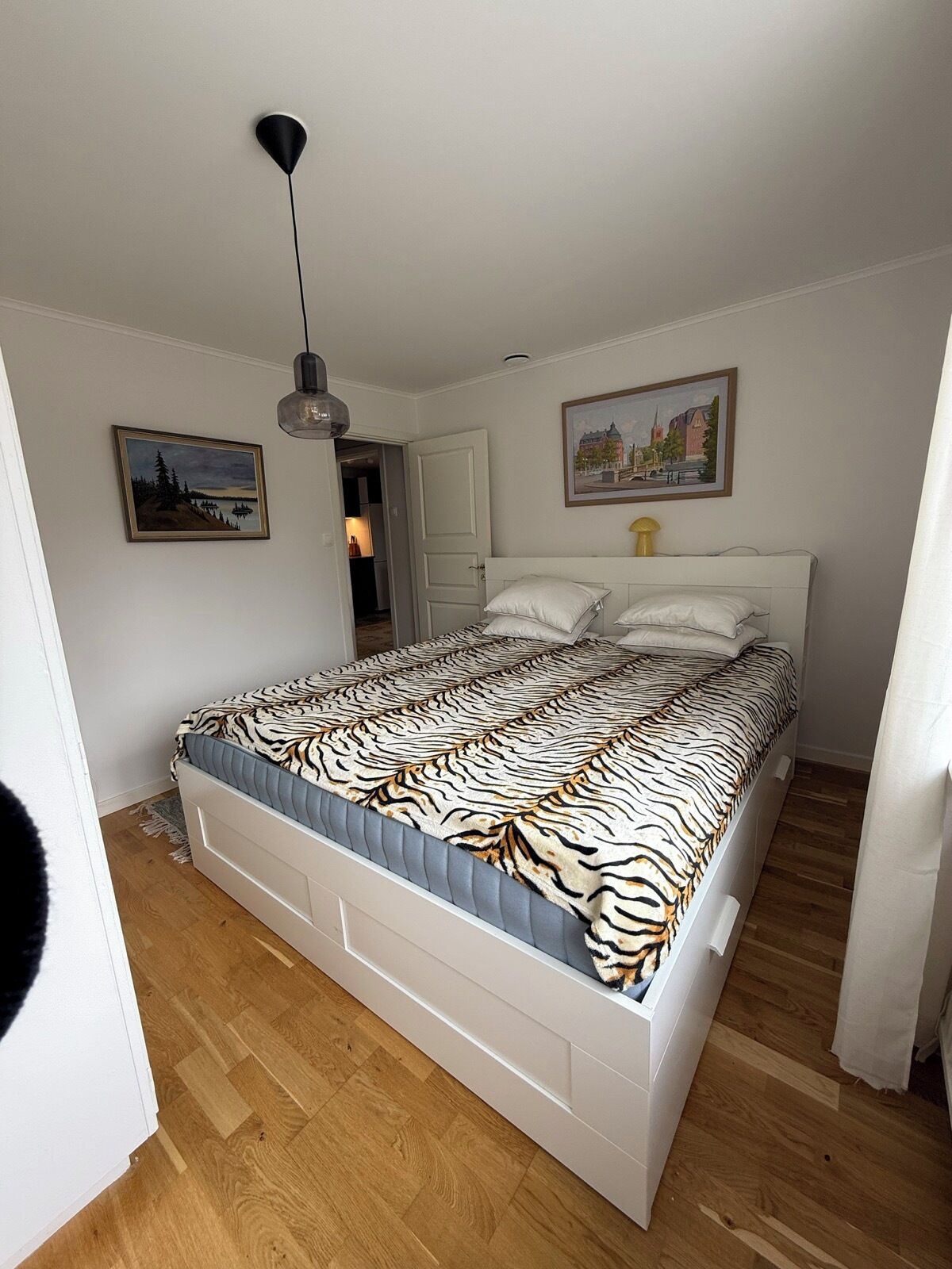 Ein Schlafzimmer mit einem Bett, einer Tür, einem Gemälde und einer Pendelleuchte.