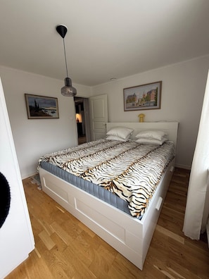 Un dormitorio con cama, puerta, cuadro y lámpara colgante.