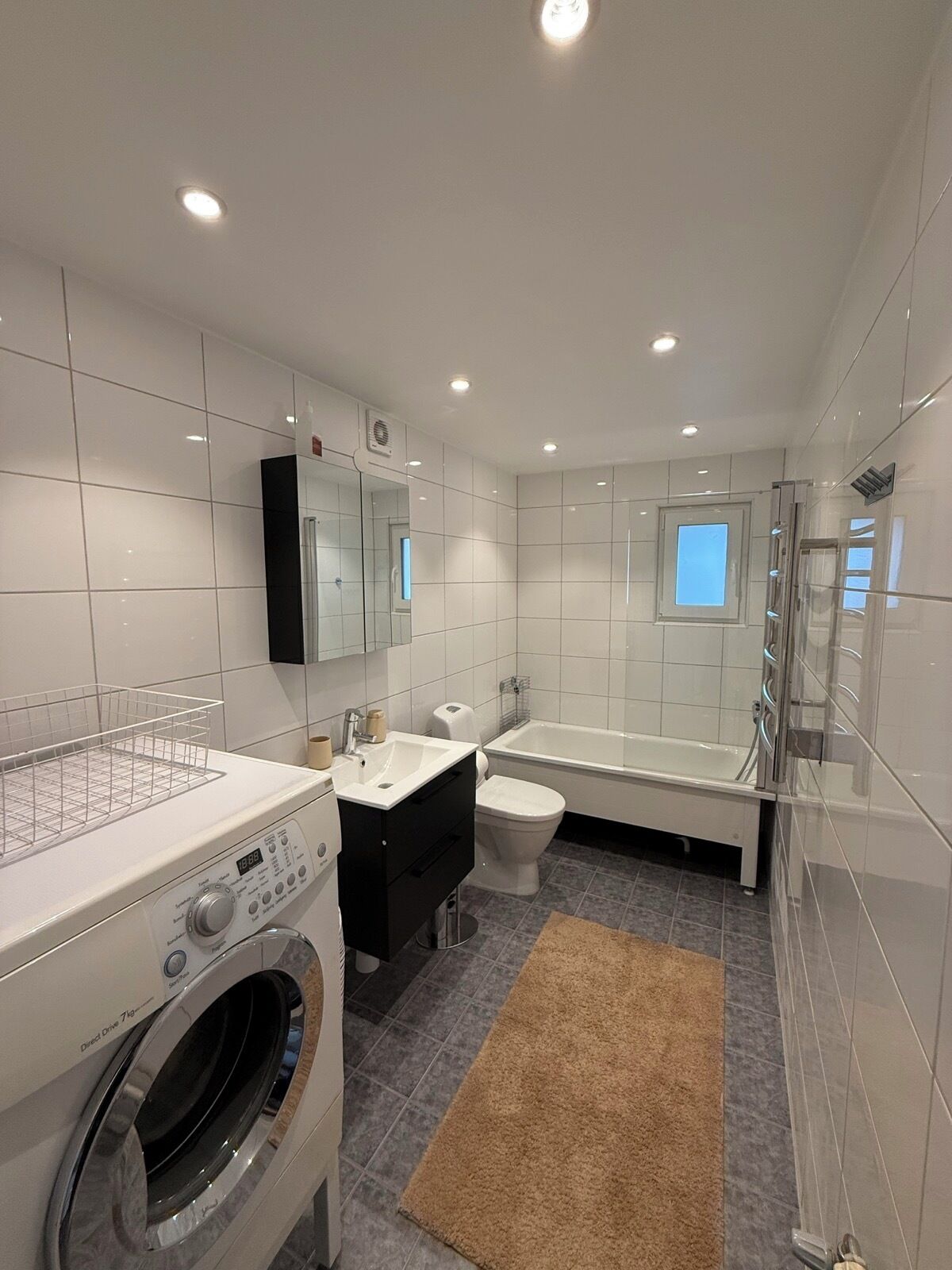 A modern bathroom with a washing machine, a toilet, a bathtub, and a shower.