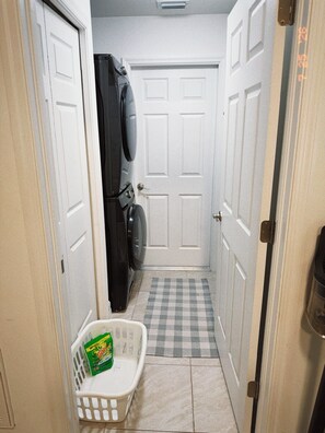 A laundry room with a washing machine, dryer, and a laundry basket with detergent. - Bessa Sol Retreat - Heated Pool & Spa - Boat parking (Cape Coral)
