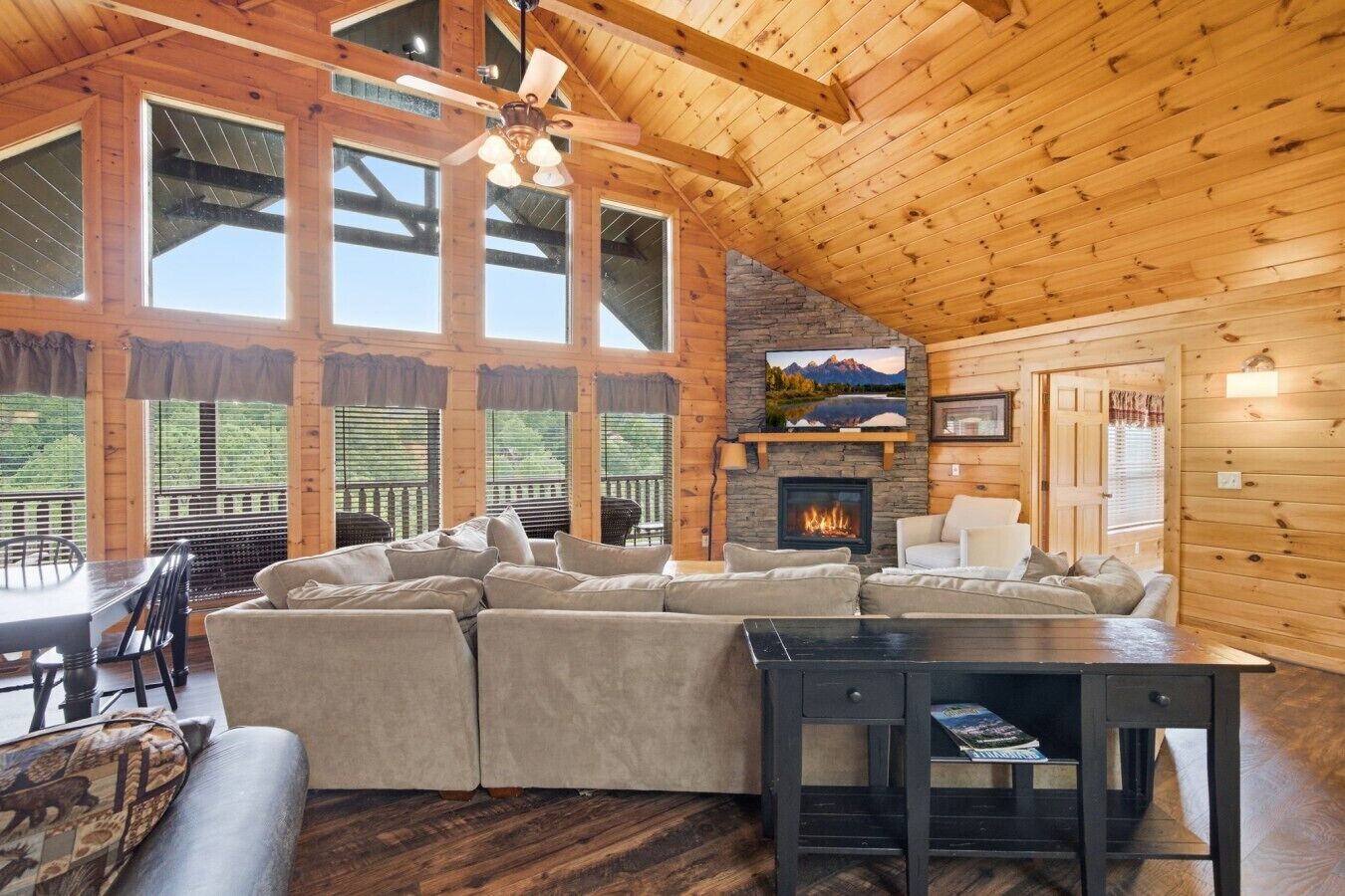 A cozy cabin interior with a large sectional sofa, a fireplace, and a dining area.