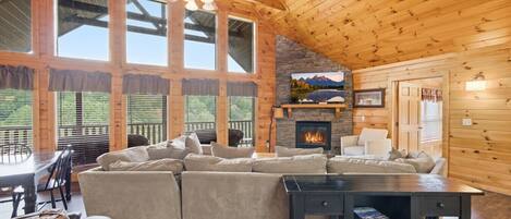 A cozy cabin interior with a large sectional sofa, a fireplace, and a dining area.