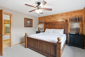 A bedroom with a wooden bed, a ceiling fan, a nightstand, and a window with blinds. - Wild Turkey | Sleeps 18! Views, Hot Tub, & MORE! (Sevierville)
