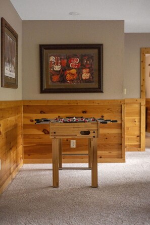 A room with a wooden foosball table, a framed abstract painting, and a door with a wooden frame. - Wild Turkey | Sleeps 18! Views, Hot Tub, & MORE! (Sevierville)