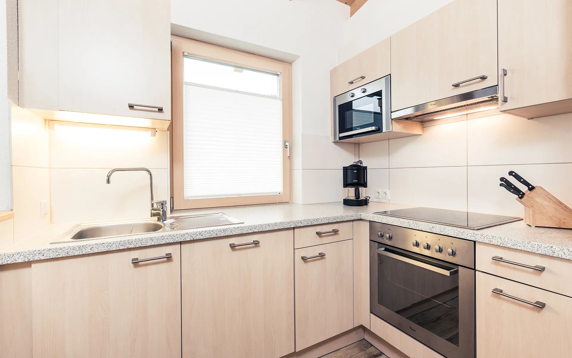 Una cocina moderna con horno empotrado, cafetera y ventana con persianas.