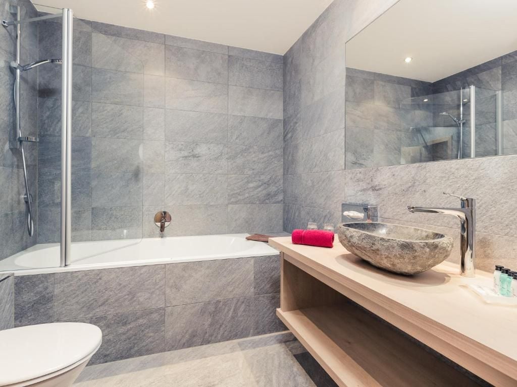A modern bathroom with a glass-enclosed shower, a white bathtub, and a wooden vanity with a stone basin.