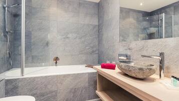 A modern bathroom with a glass-enclosed shower, a white bathtub, and a wooden vanity with a stone basin.