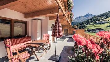 An outdoor patio with wooden furniture, a striped umbrella, and a view of mountains.