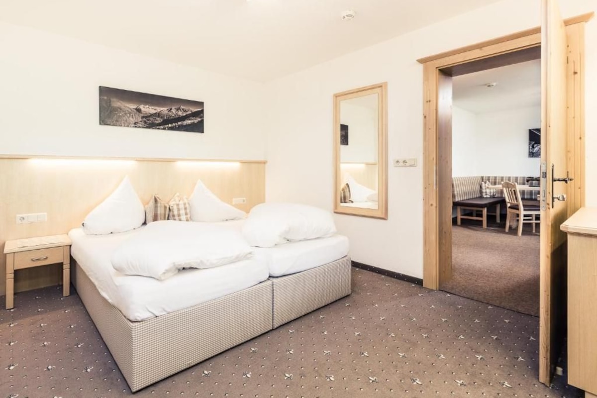 Een hotelkamer met een bed, een nachtkastje, een spiegel en een deur naar een eethoek.