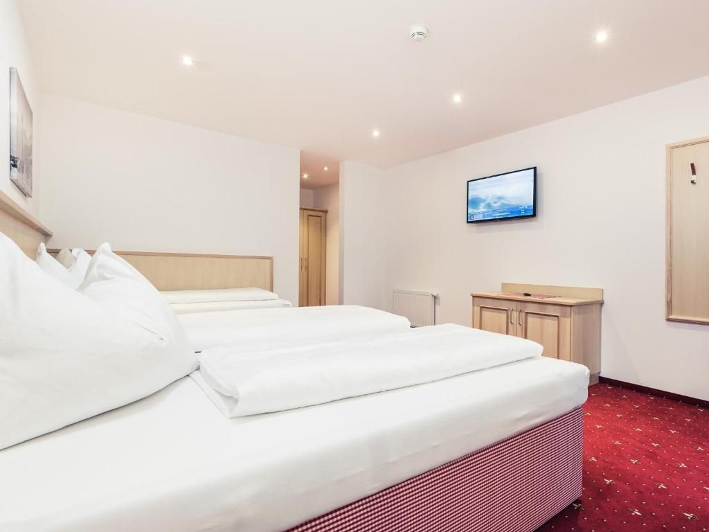 Habitación de hotel con dos camas, un televisor, un escritorio pequeño y alfombra roja.